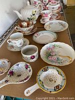 Overall display of Royal Albert tea cup luncheon set, teapot, tea rests, and strainers with floral and gold accents.
