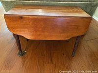Full view of antique hardwood drop leaf table showing closed leaves, hardwood top and carved legs.