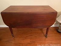 Front view of closed drop leaf table showing mahogany wood surface and overturned legs with casters.
