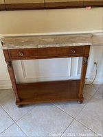 Full view of the front of the console table showing the marble top, drawer with two round metal pulls, wooden legs and lower shelf.