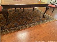 Full view of the wool rug under dining table showing peach ground with floral pattern in beige, blue, and black.
