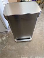 Front view of Simplehuman large trash can, showing rectangular shape, stainless steel body, and black pedal at base.