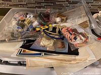 Overview of the entire lot showing multiple plastic bags with sewing supplies scattered on kitchen counter including spools of thread and fabric pieces.