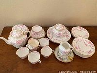 Photo showing full tea set including teapot, sugar bowl, creamer, rims of plates, and cups lined up