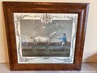 Framed aquatint engraving print depicting a gray horse and a man with detailed ornamental border and crest on top.