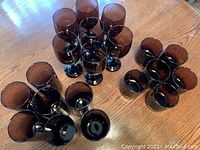 Overhead view of the 20 purple drinking glasses arranged in clusters on a wooden table, showing the tall, short, and wine glass variations.
