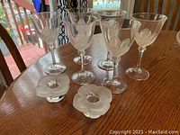 Six crystal wine glasses with frosted floral patterns on the bowl, displayed in a group with two frosted glass flower-shaped candle holders on a wooden table.