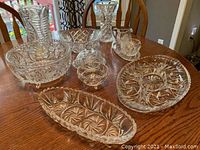 Photo showing assortment of pinwheel pattern crystal glassware including vases, bowls, cream and sugar set, and divided trays arranged on wooden table.