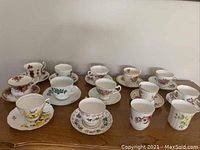 Photo of eleven bone china tea cups and saucers with floral patterns, arranged in two rows on a wooden surface.