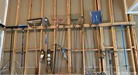 Photo shows various garden tools including rakes, shovels, and brooms hung on wood-framed hooks.