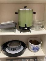 Green coffee urn on shelf with glass baking dishes and cake pans below