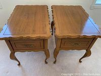 Two matching walnut French Provincial end tables with drawers and decorative metal hardware on carpeted floor.