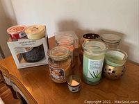 Assortment of candles including jar candles, votive, floating candles, and a boxed Yankee Candle Scenterpiece wax warmer with wax tarts on a wooden surface