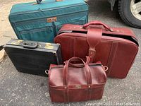 Photo of all four items: three suitcases and one leather briefcase arranged together outdoors on a paved surface.