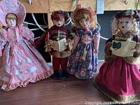 Four dolls displayed on a wooden surface, showing full outfits and faces