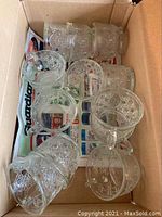 Twelve clear glass cups with textured circular patterns arranged in a box showing the set of cups
