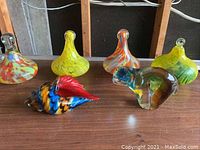 View of all six handblown glass decor items on wooden surface: four teardrop-shaped ornaments in vivid colors and two animal-shaped figurines, one bird-like and one abstract.