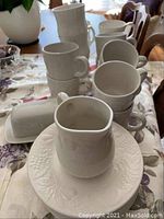 Photo of white cups and saucers with embossed floral texture and matching butter dish and creamer on a table.