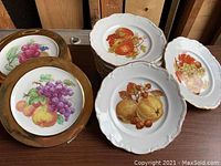 Two sets of luncheon plates, one with gold band and fruit designs including grapes and pears, the other with gold trim and multiple fruit designs with scalloped edges.