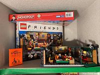 Photo showing LEGO Friends set with mini-figures arranged in a cafe scene, Monopoly box, and Gypsy Witch cards box.