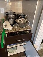 Kitchen appliances and cookware set placed on countertop and in drawer, showing Crockpot, blender, toaster, hand mixer, mixing bowls, pots, pans, and silverware.