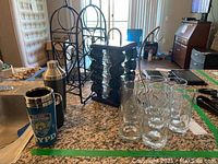 Photo of the barware including wine racks, glass bottle holder, cocktail shaker, travel mug, and glasses on kitchen counter