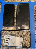 Two black iPhones placed side by side on a granite surface, one with cracked screen, one intact, showing front view.