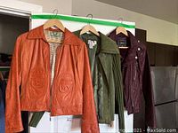Three women's leather jackets hanging on wooden hangers to show colors, styles, and design details.