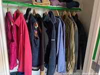 Ten women's jackets hanging on a green rod, showing variety in style and color including pink, navy, black, tan, and gray