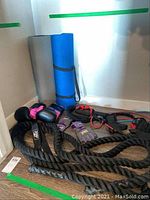 Photo showing black and pink boxing gloves, black braided fitness ropes, purple fingerless workout gloves, and rolled blue and gray exercise mats.