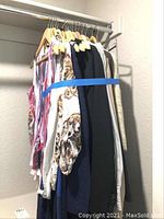 Wide view of multiple women's clothing items hanging on wooden hangers, showing variety of styles and colors including sweaters, button-up shirts, and dresses.