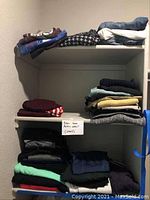 Shelves with folded women's clothing including sweaters, t-shirts, and activewear size small