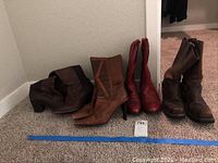 Three pairs of women's boots arranged in a corner against a wall on carpeted floor