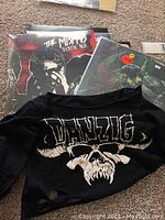 Photo shows Danzig concert shirt with skull design placed on the floor with vinyl records behind it.