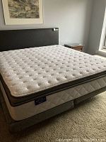 King size mattress with quilted white top and gray border over split box springs on carpet