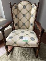 Full front view of wooden rocking chair upholstered in cream fabric with green and blue floral pattern