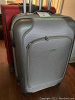 Grey Samsonite hard shell suitcase with black and grey textured surface and retractable handle, standing in front of red luggage.
