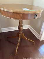 Front angled side view of the round wood table showing pedestal leg base and drawer with metal pull.