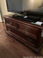 Full view of mahogany wood TV stand with a flat screen TV on top. Traditional style with decorative drawer fronts and metal handles.
