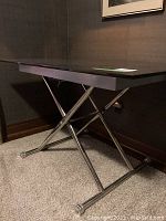 Side view of the black tempered glass desk showing the chrome X-shaped legs and adjustable height feature.