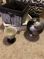 Photo showing the large gray wicker basket with black fabric lining, small white wicker basket, black globe and patterned glass votive arranged on carpet.