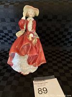 Front view of Royal Doulton 'Top of the Hill' porcelain figurine showing seated woman in red dress and hat.