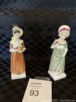 Two Royal Doulton porcelain figurines, Ruth HN 2799 and Louise HN 2869, displayed on a checkered fabric background.