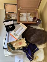 Overview of the gentlemen's lot showing humidor with accessories inside, pocket watch in box, Dockers handkerchiefs, cufflinks box, brown suede hat, sunglasses and some vintage collectibles.