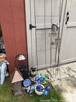 Photo of assorted garden decor, bird feeders, and plant pots arranged on ground against shed