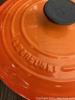 Top view of orange lid with embossed Le Creuset logo and black knob