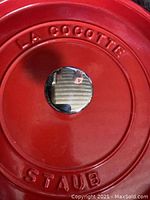Top-down view of red lid embossed with ‘LA COCOTTE STAUB’ and stainless steel knob