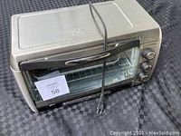 Front and top view of the Hamilton Beach toaster oven showing control knobs, glass door, and power cord wrapped around the unit.