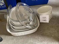 Stacked assortment of white CorningWare baking dishes with glass lids and small bowls to the side.