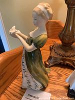 Side view of Royal Doulton 'Veneta' figurine showing woman holding a bird, wearing long dress with floral design.